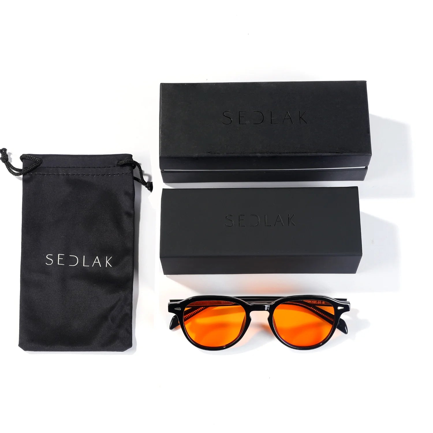 Sunglasses with orange lenses beside two black cases and a pouch with 'SEDLAK' branding.