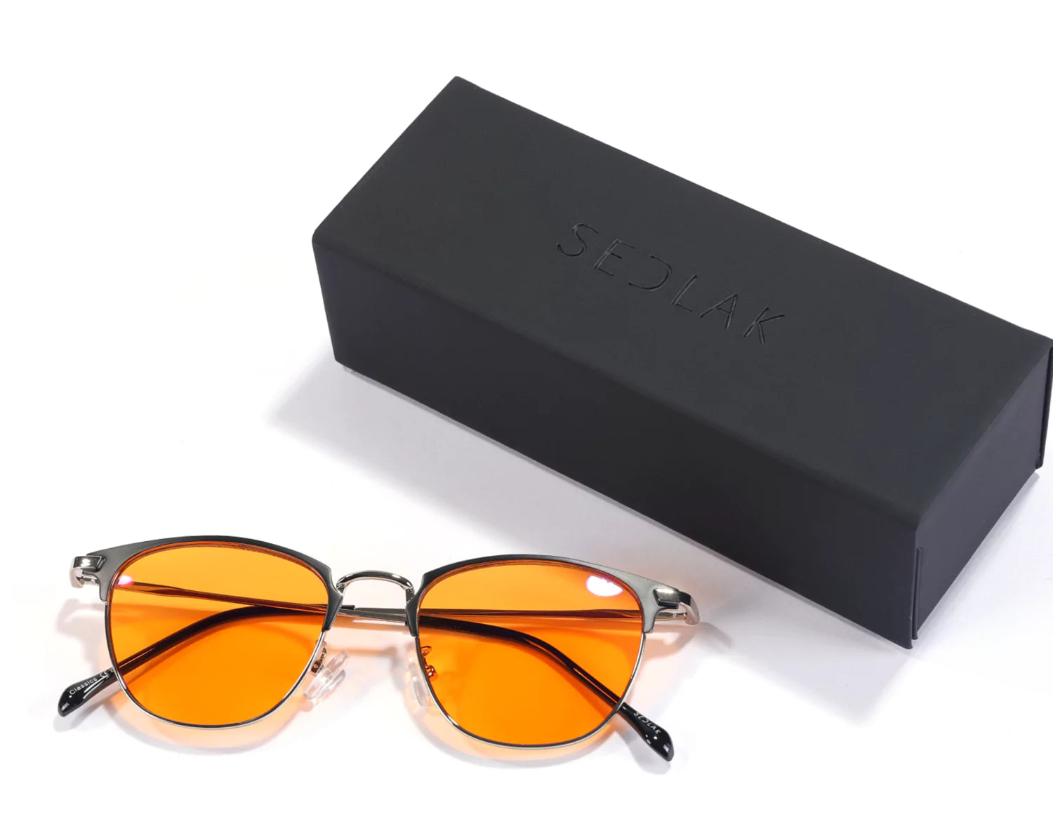 Orange-lensed sunglasses next to a black box with 'SEDLAK' embossed on it.