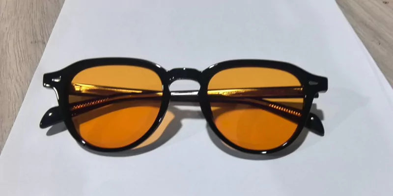 Black framed sunglasses with orange tinted lenses on a white surface.