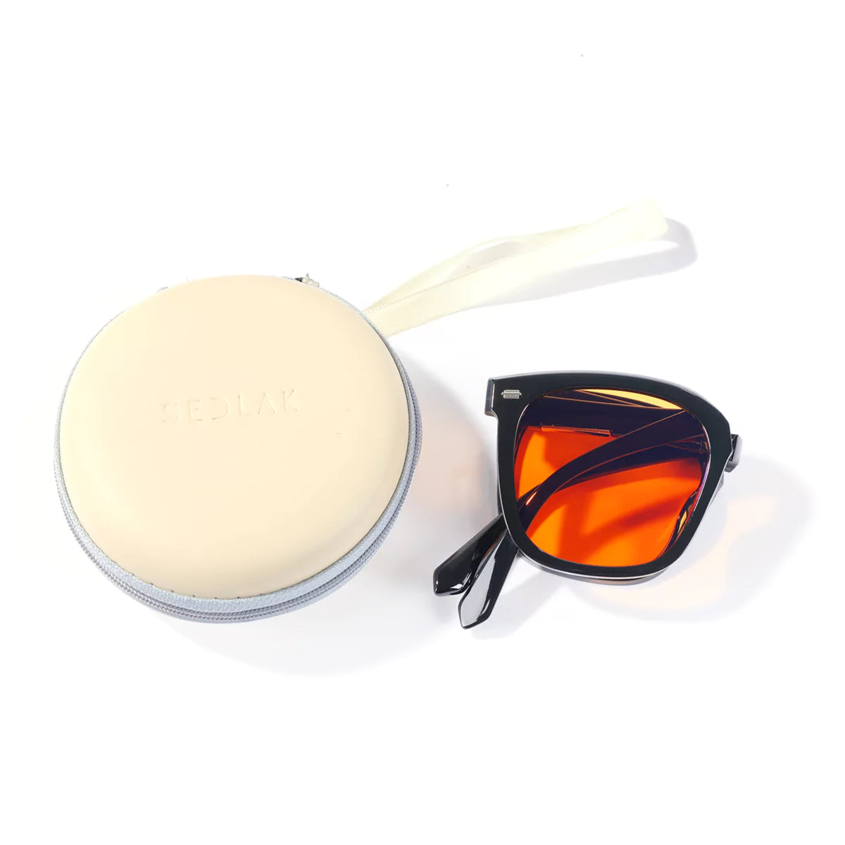 Sunglasses with orange lenses next to a round case.
