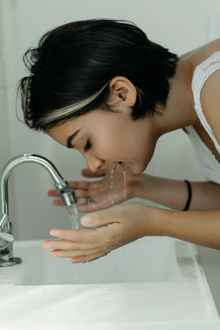 femme avec les cheveux courts noirs est au-dessus de lévier et fait couler de l'eau du robinet, elle veut prendre l'eau avec ses mains