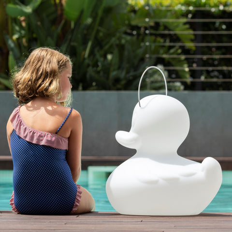 A girl sits next to the DUCK-DUCK lamp by the swimming pool