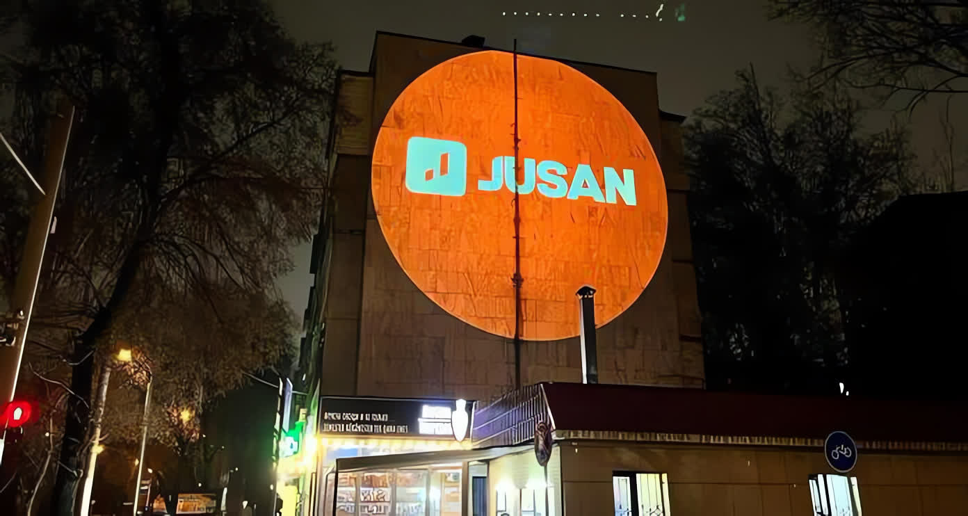 Jusan brand logo illuminated on a city building at night by a One Gobo 300W projector, showcasing impactful urban advertising.