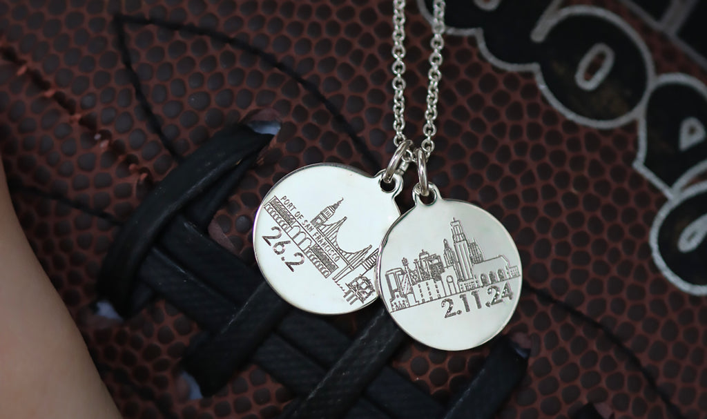 silver necklaces engraved with K.C. and S.F. city skylines in front of a football