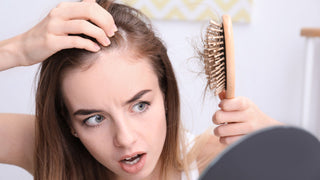 A woman who is losing her hair looks worriedly at the brush with her hair stuck to it