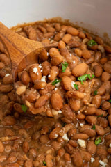 Crock Pot Pinto Beans being served with a wooden spoon in a serving bowl.