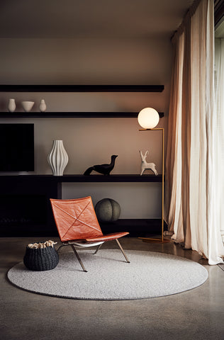 Grey circular rug with orange chair and black shelf