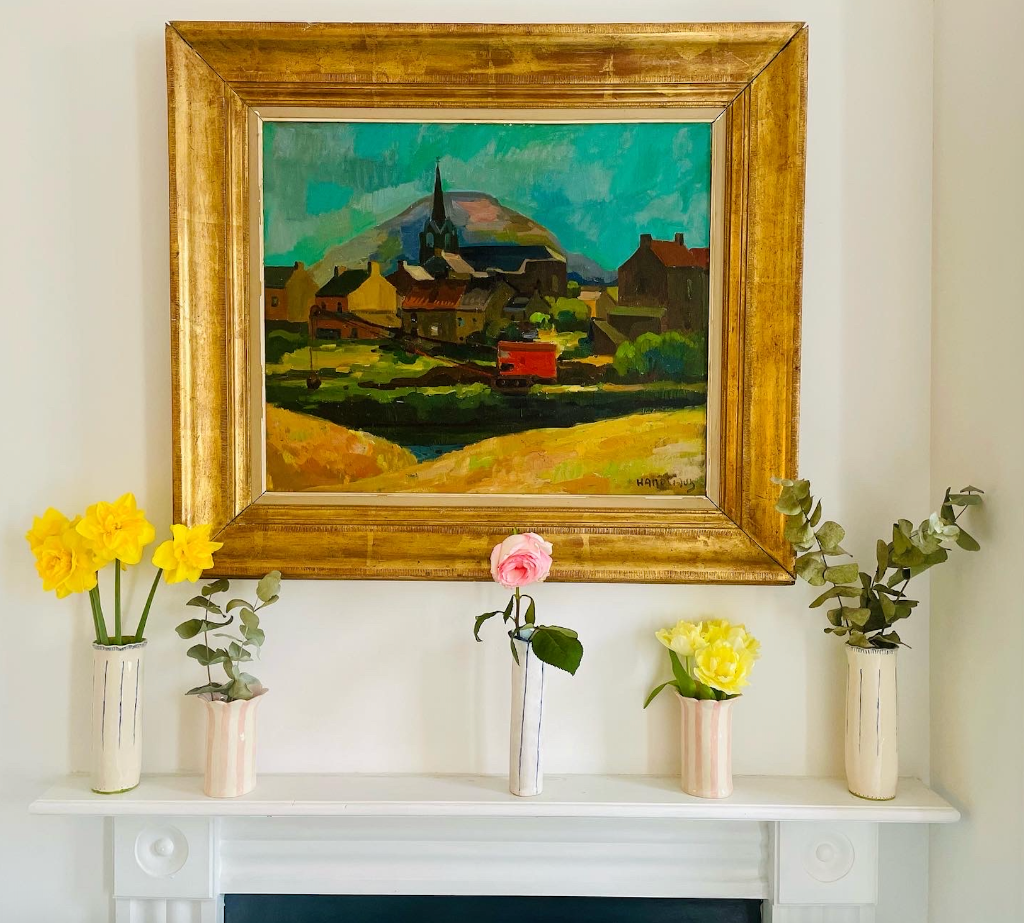 a large golden framed oil painting sat on the mantel behind a collection of hand crafted ceramic vases