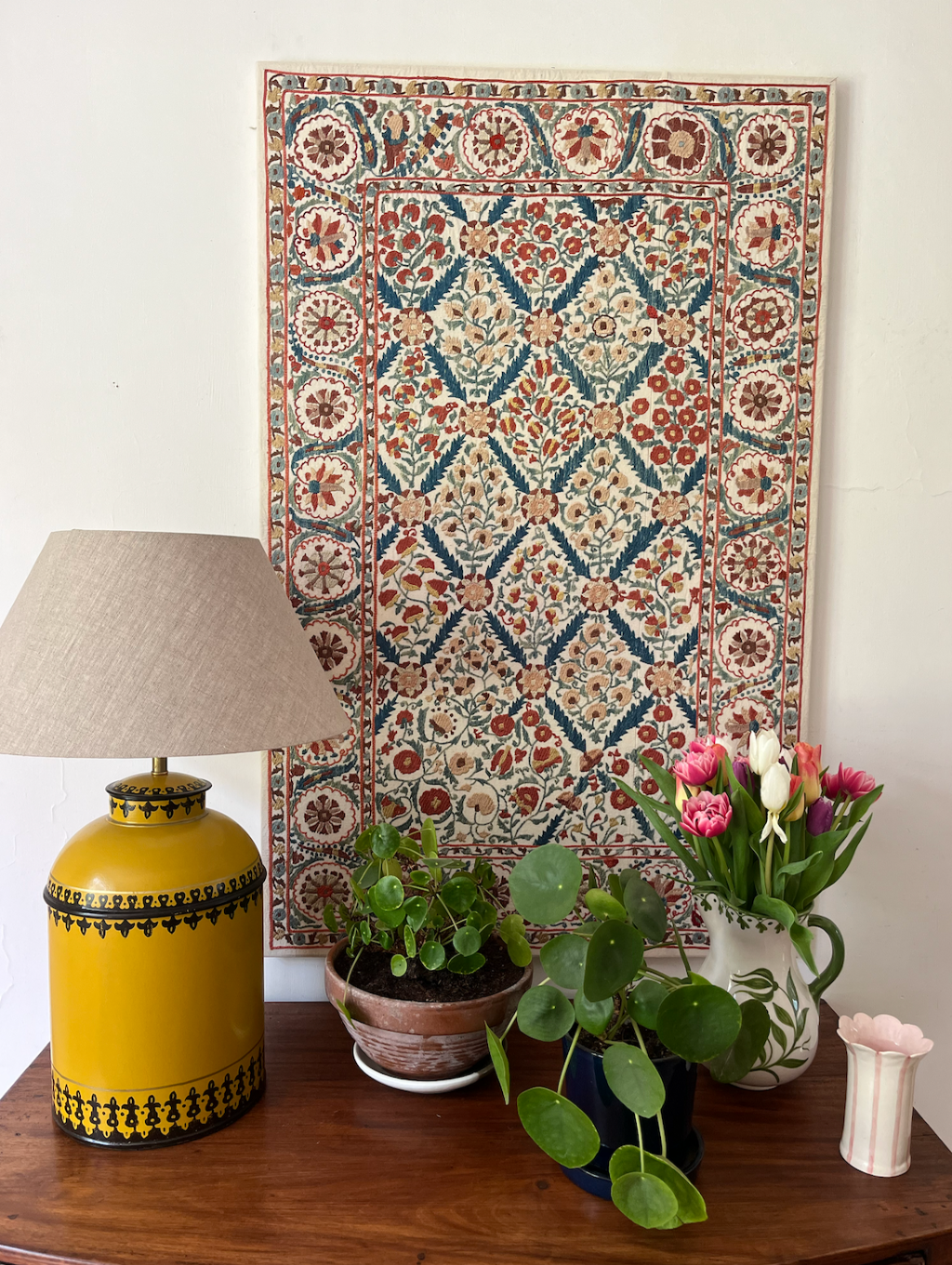 a stretched vintage suzani fabric dispalated behind a console table with potted plants