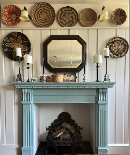 A blue fireplace in a panelled room showcases a section of candles, lamps and decorative baskets