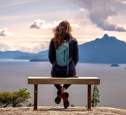 Woman sits on a bench over looking Howe Sound in Squamish after a hike up mountains