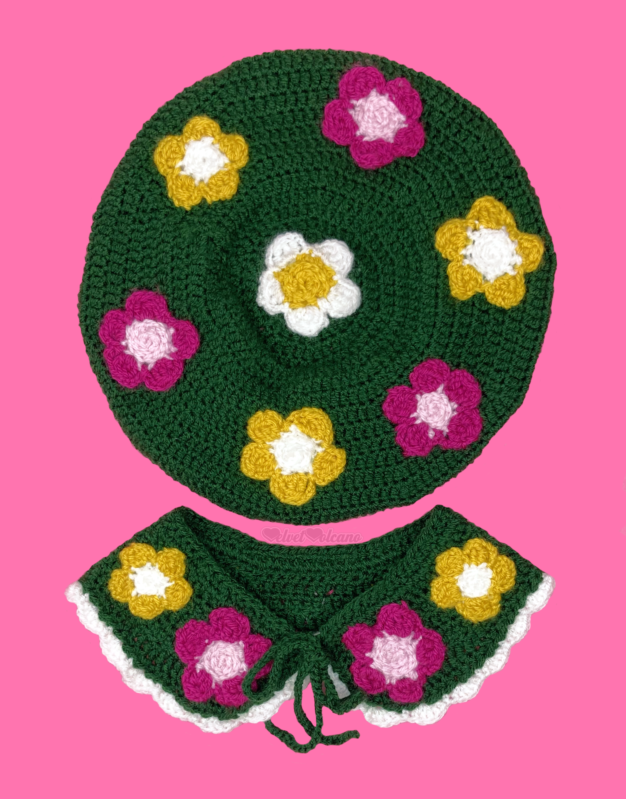 A dark forest green crocheted beret and Peter Pan collar set. Both items feature mustard yellow and white and dark raspberry pink and baby pink flower appliques. The collar also features a white frill trim around the bottom edge.