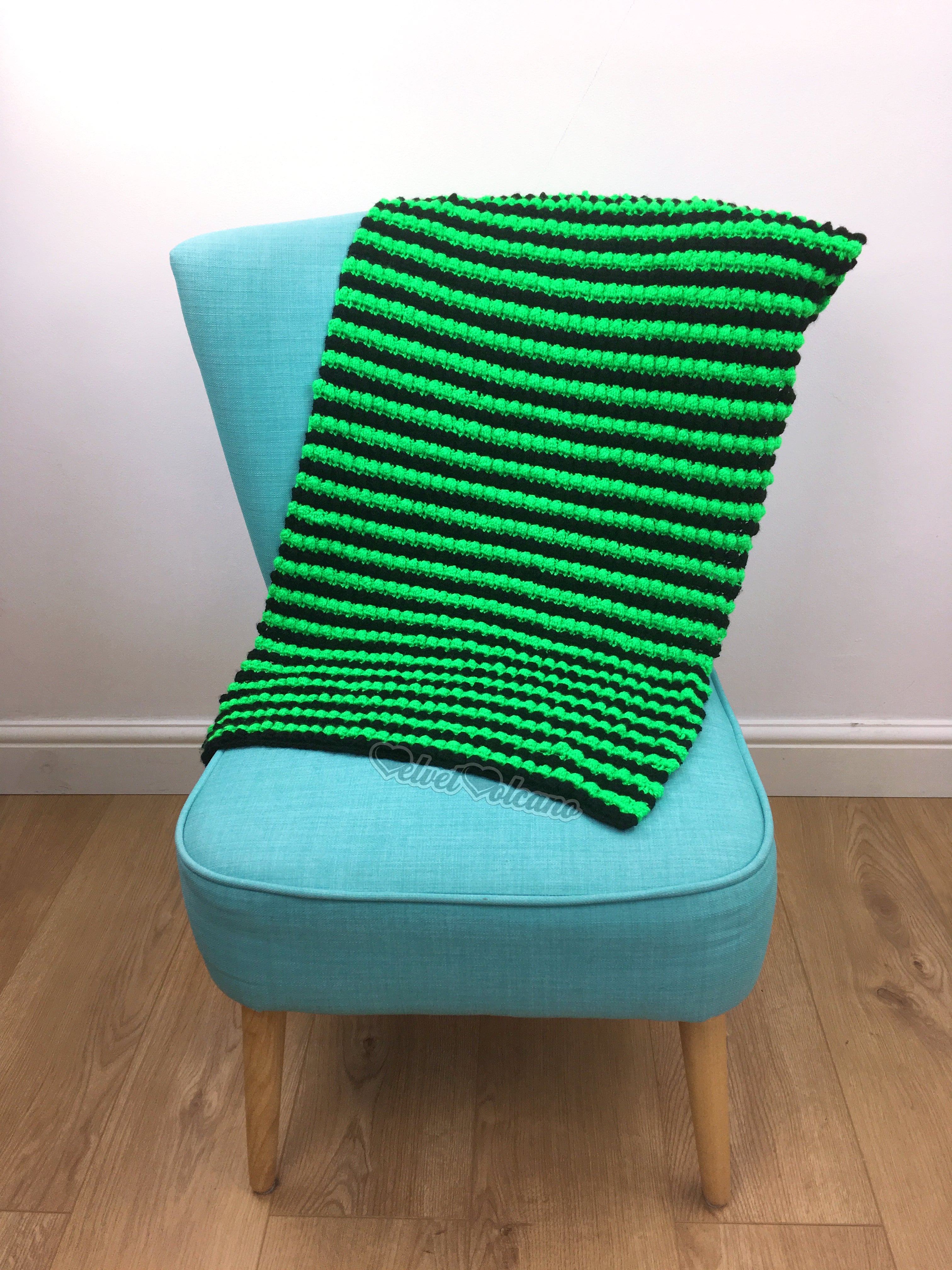 A neon green and black striped crocheted blanket, laid over a turquoise chair.