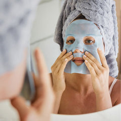 Woman applying a bio-cellulose sheet mask on her face