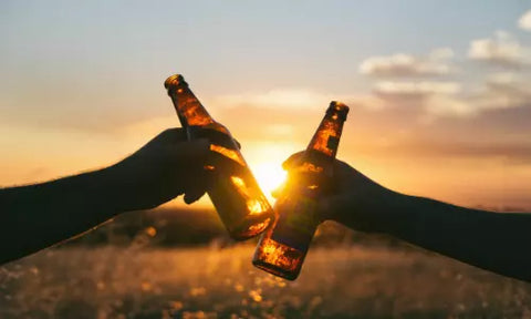 Anstoßen mit Bierflaschen bei Sonnenuntergang