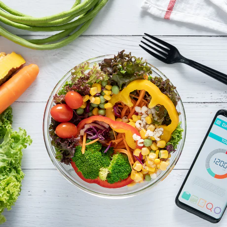 Bunte Gemüsebowl mit Handy mit Kalorienangabe im Hintergrund