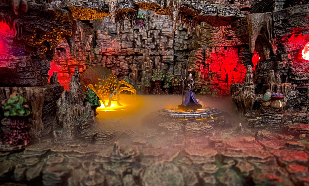 Dark Elf High Priestess and Arachnika the spider oracle stand at the center of the cavern, fog rolls across the cavern floors.