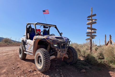 Image of a Yamaha RMax UTV/SXS featuring the GBC Parallax tires. This UTV is on a desert trail next to a wooden arrow signs pointing in different directions, labeled with the respective trail.
