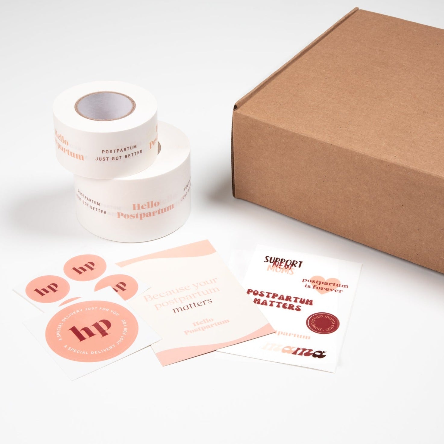 Branding materials with 'Hello Postpartum' theme, including stickers, tape, and a cardboard box.