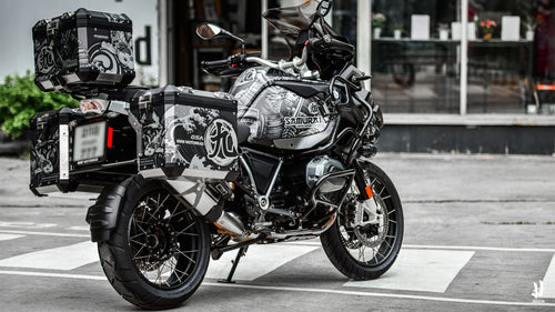 A BMW R1250 GS Adventure in a monochrome Samurai-themed custom design with detailed pannier graphics.