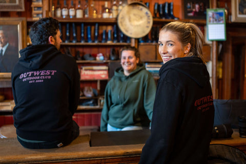 Three people in a pub wearing Outwest Hoodies, rear logo visible