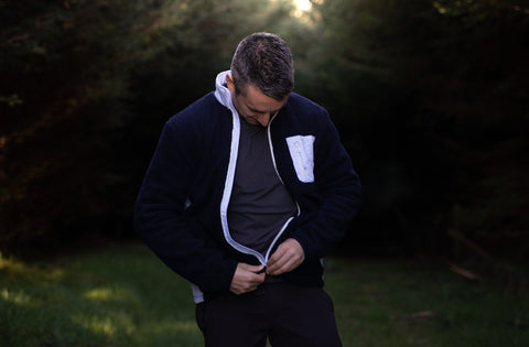 Man zipping up his Farraige fleece in forest