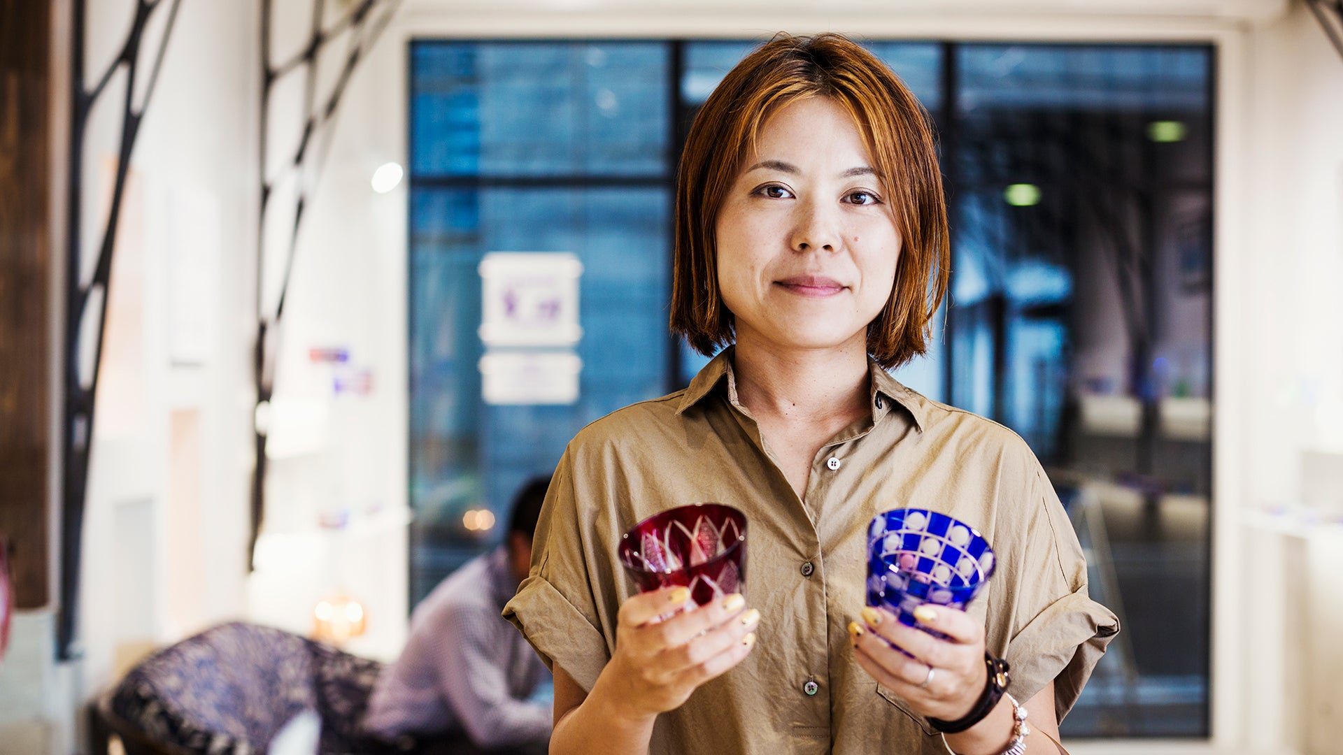 Glass artisan in studio holding etched colored glass cups