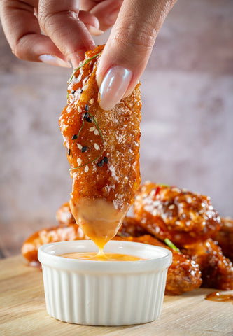 person dipping a chicken wing into buffalo sauce
