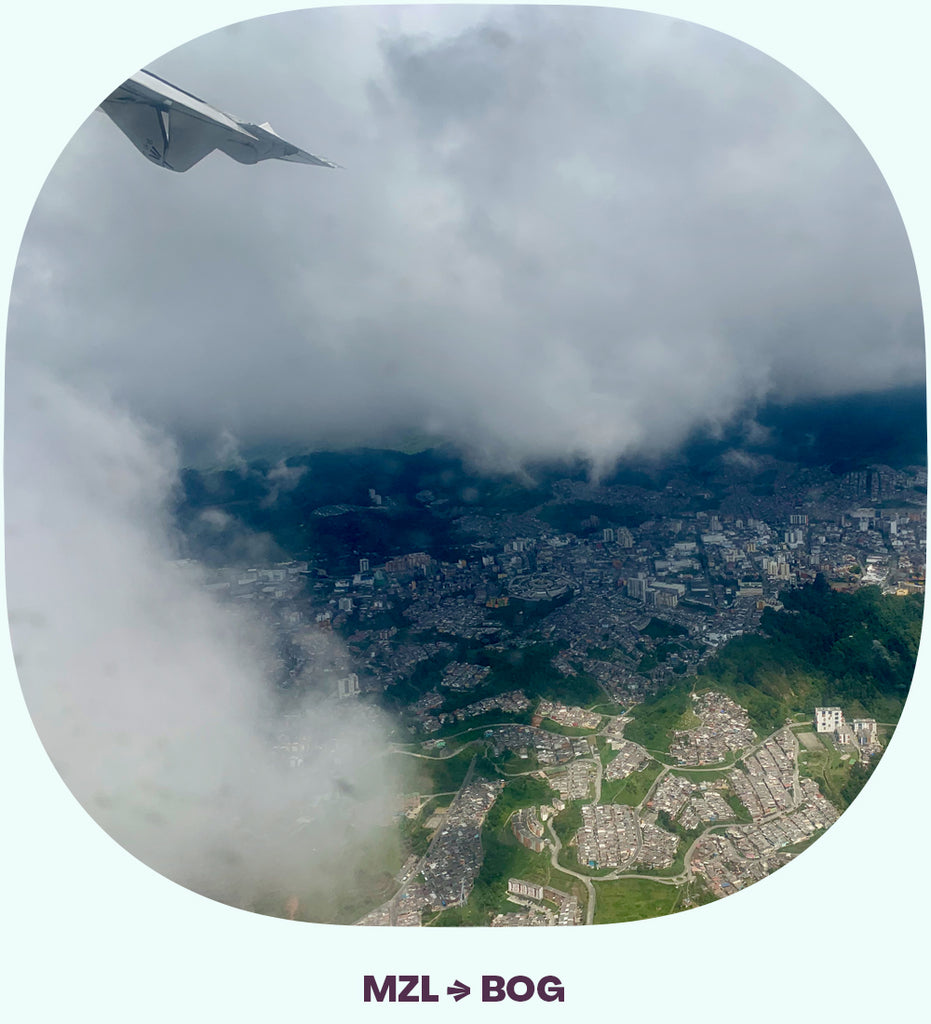 An airplane wing going into the clouds, with a peek of a town visible through the clouds.