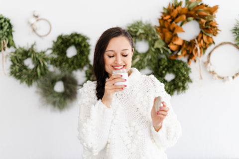 woman smelling holiday candle in front of wreaths on the wall 