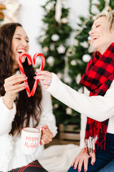 two women at christmas making a candy cane heart while laughing