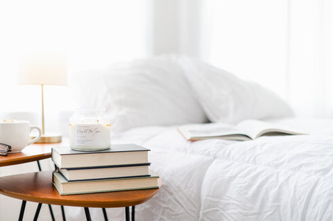 candle burning on a stack of books on the bedroom nightstand. Book lies open on the bed. 