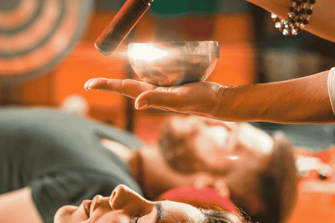 Tibetan Sound Bowl being played above two peoples heads while they lie down