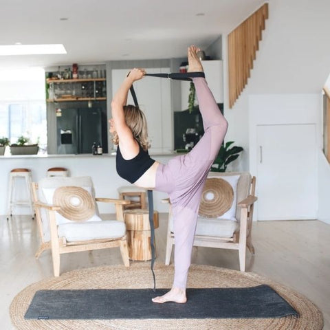 Woman balancing in one leg using strap to stretch other leg over head