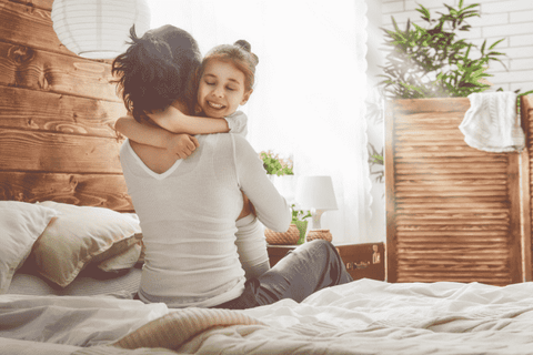 Woman sat on edge of bed hugging child