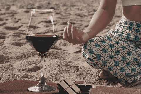 Woman in crossed legged meditation pose next to a glass of red wine