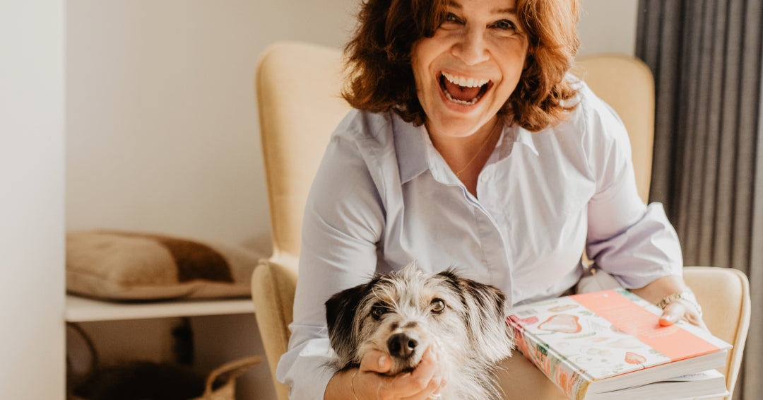 Ingrid met hondje Lou op een stoel bij haar thuis lachend in de camera