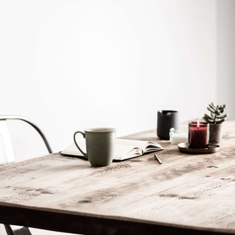 Wooden table in a white room with a mug, notebook and candle