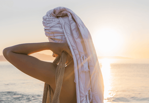 Women at the beach by the sea wears a Pomp & Sass grey white body towel as a hair wrap after swimming. the sun sets 