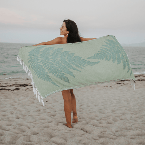 Woman standing on the beach while holding a Turkish towel behind her.