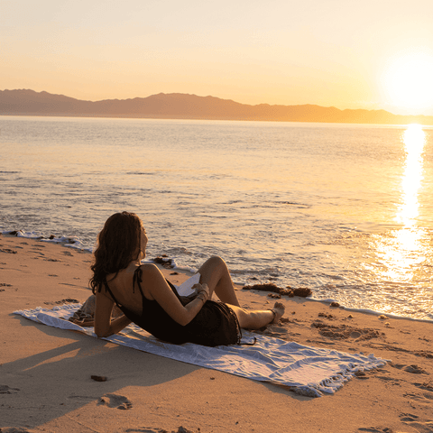 Woman on a beach with a Turkish towel at sunset