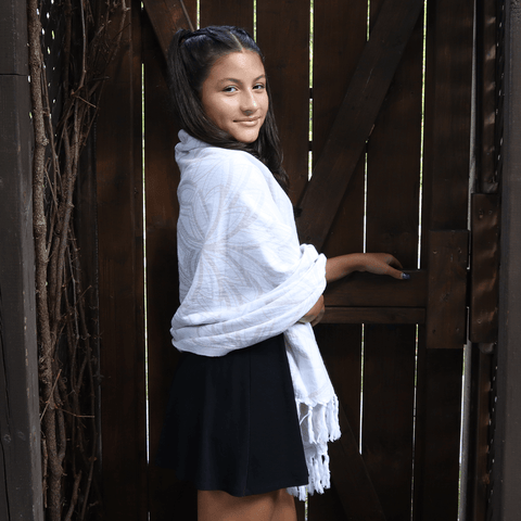 Latina girl standing beside a door with her hand on the handle, looking over her shoulder. White Pomp & Sass Turkish towel draped over her shoulders. 