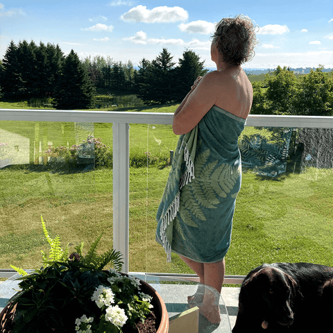 Elderly woman outdoors wrapped in a green leaf Pomp & Sass Turkish towel looking into the distance on a sunny day.