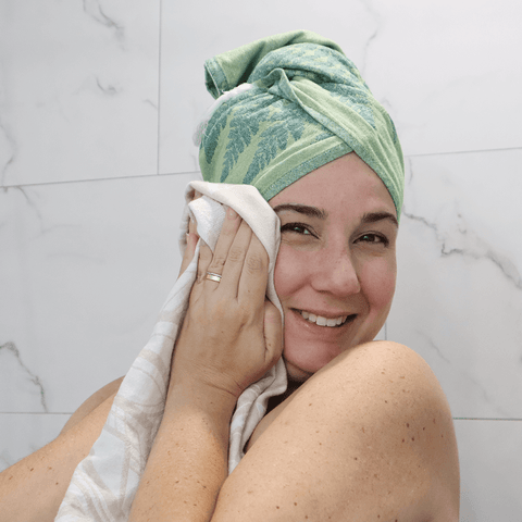 Woman in the shower with a green Turkish towel around her head and a white Turkish towel drying her body