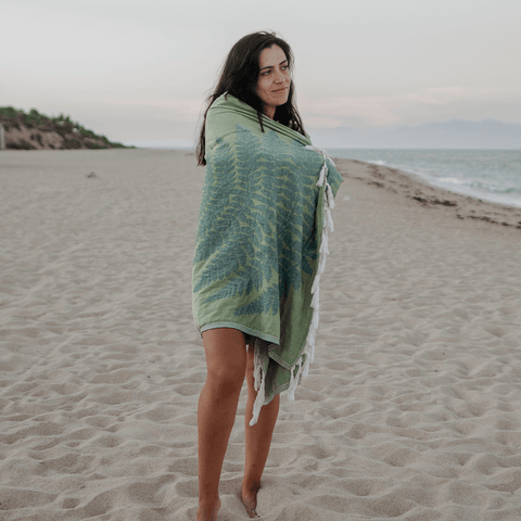 Young woman on a beach wrapped in a green fern Turkish towel smiling