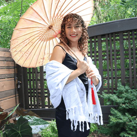 Young Latina woman holding a parasol, draped in a white Turkish Towel.