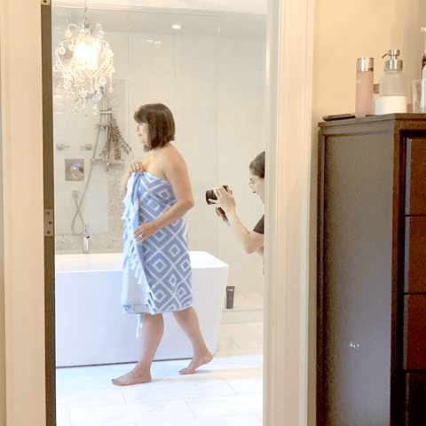 Woman wrapped in a blue diamond patterned Pomp & Sass Turkish towel while a lady photographs her.