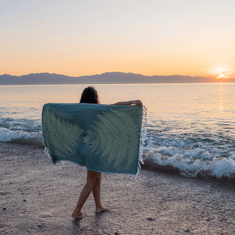 Woman at the beach by the water with a green fern Turkish towel