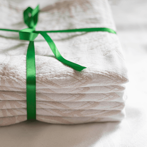 A stack of oat and white Turkish towels wrapped in a green satin bow