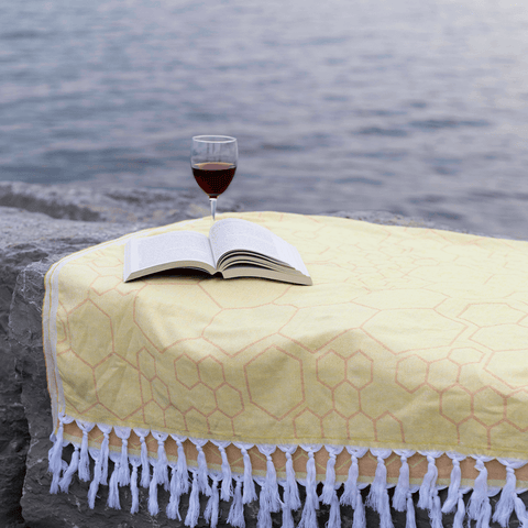 A yellow Pomp & Sass Turkish towel used as a picnic blanket by the lake, a bottle of wine and a book on the towel.